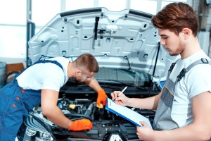 Running diagnostics. Two handsome car mechanics in uniform checking the engine under hood in the car service station and checking in service order