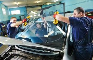 Automobile glaziers workers replacing windscreen or windshield of a car in auto service station garage